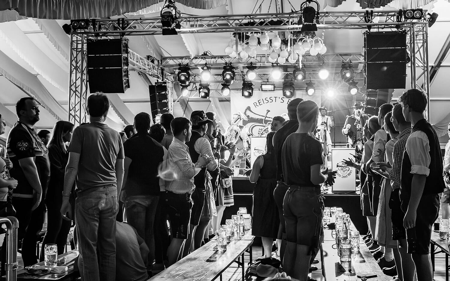 Schwarz-Weiß-Aufnahme von Menschen auf Bierbänken vor der Bühne