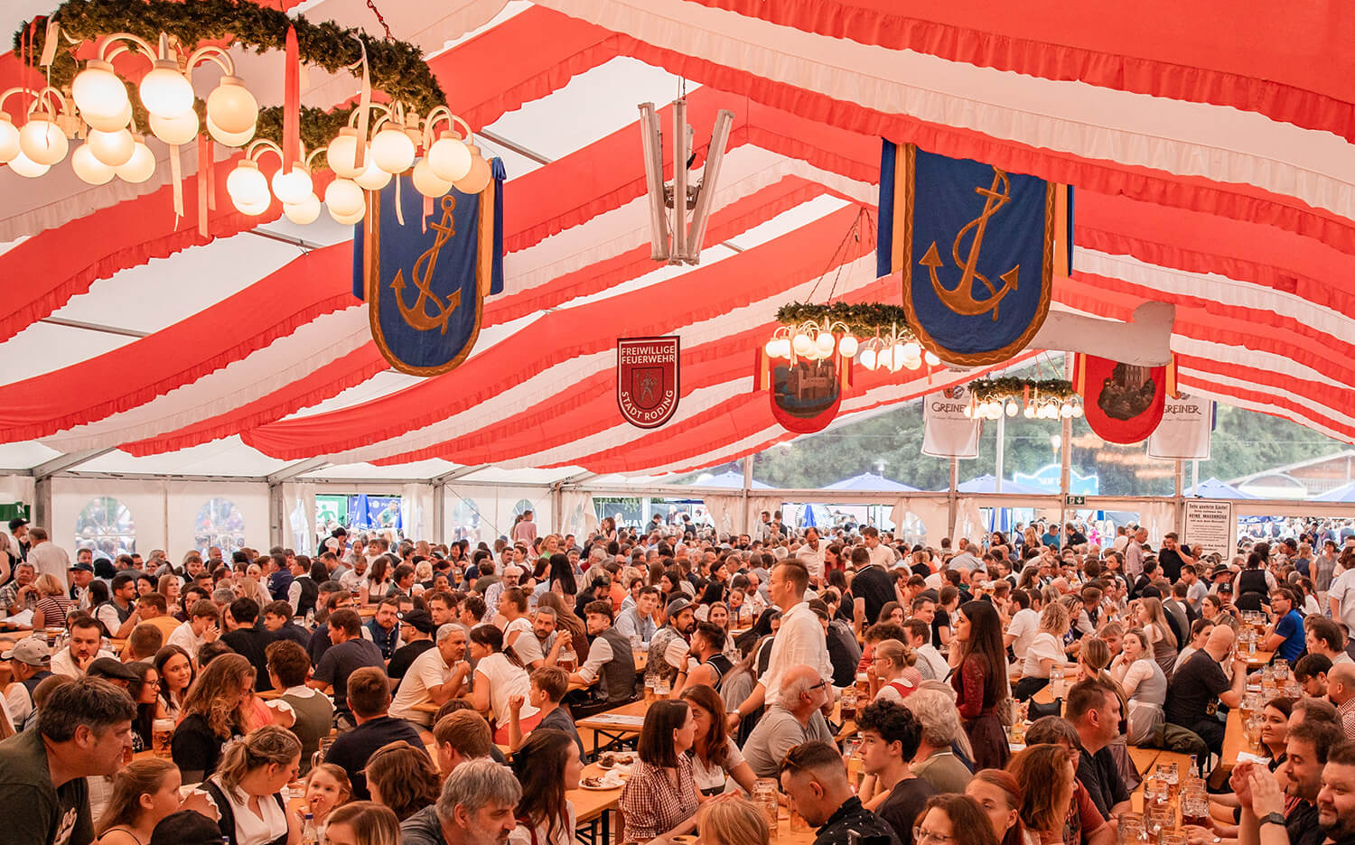 Menschen sitzen in einem gut gefüllten Bierzelt und feiern gemeinsam bei ausgelassener Stimmung.